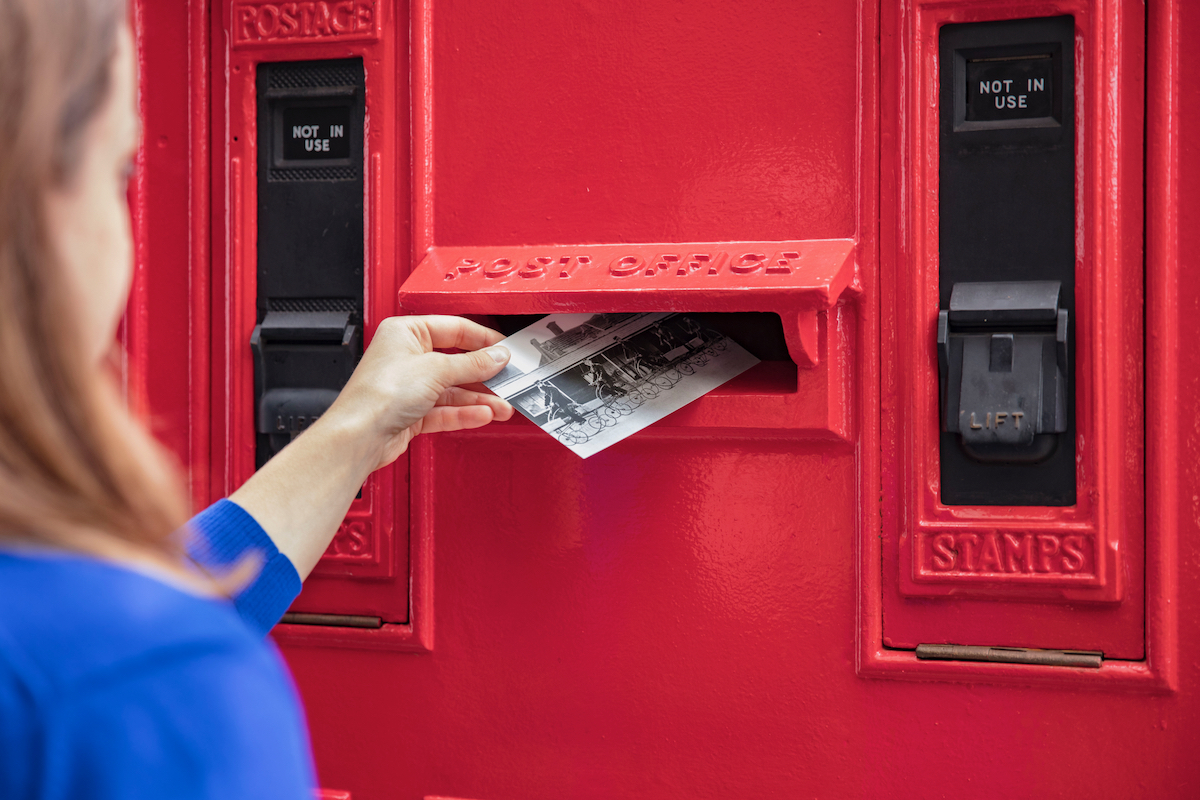 Posting a postcard in a red post box